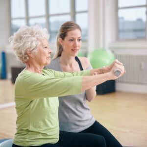 Young instructor guiding elderly woman in exercise with a resistance band.