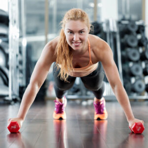 Woman doing push-ups with dumbbells in a gym.