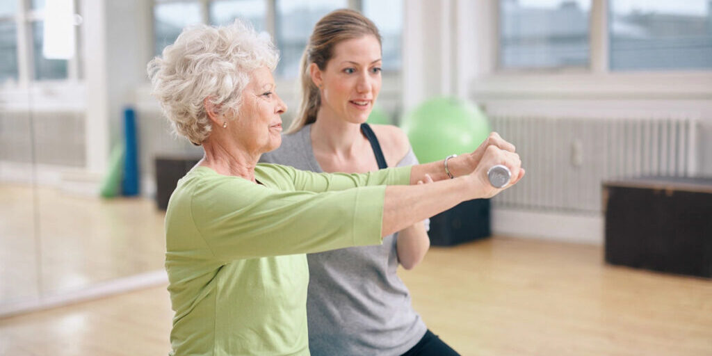 Young instructor guiding elderly woman in exercise with a resistance band.